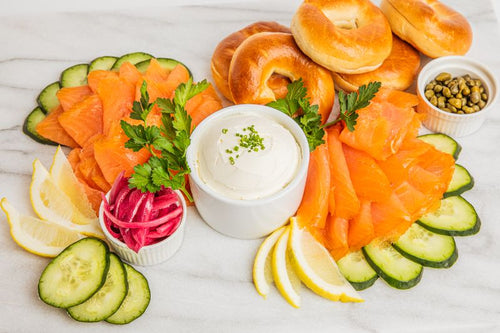 Platter of smoked salmon, sliced cucumbers, lemon wedges, cream cheese, pickled onions, and capers, with mini bagels 
