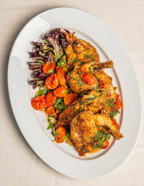 Roasted chicken breast on platter served with blistered tomatoes and kale