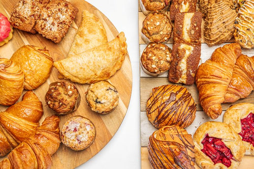 Pastries including croissants, danishes, mini loaves, muffins, and galettes, displayed on wood boards