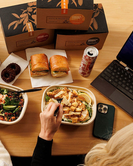 Two people eating at a table with food, drinks, and a laptop.