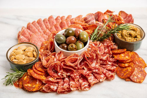 Assorted cured meets on a platter, with cups of almonds, olives, and mustard