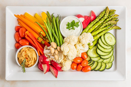 Ceramic platter with assorted veggies, with cups of hummus and tzatziki