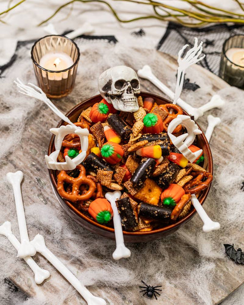 Snack mix with chex, pretzels, candy corn and pumpkins, with Halloween decorations of bones and bats