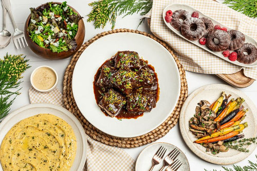 Platters of short ribs, creamy polenta, roasted carrots, and mini bundts, with a mixed greens salad, all part of a package meal