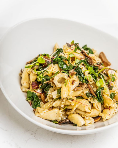 Serving bowl of campanelle pasta with mixed mushrooms and wilted spinach