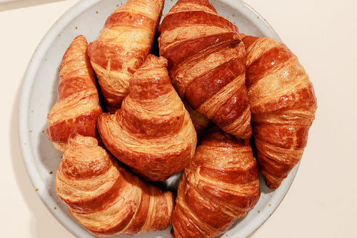Pile of butter croissants stacked on a round white plate 