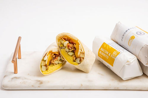 Wrapped breakfast burritos on a marble tray - one burrito sliced in half exposing the fillings