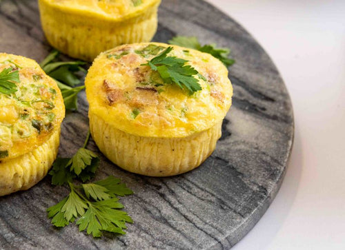 Individual baked egg frittata with herb garnish, on a dark wood platter