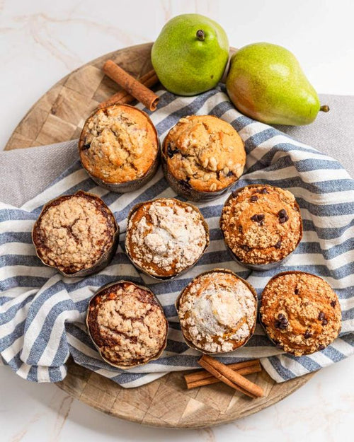Assorted muffins on a wooden board, covered in striped linen. With pears and cinnamon as accessories