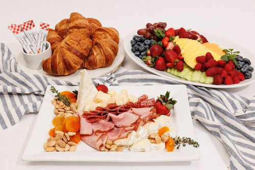 Breakfast package on ceramic platters including croissants, fresh fruit, ham, nuts and cheese