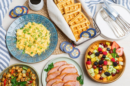 Breakfast package with waffles, scrambled eggs, fresh fruit, sliced ham, and potato hash
