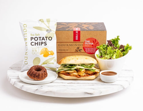 Boxed lunch including sandwich, mixed greens salad, potato chips, and mini chocolate dessert