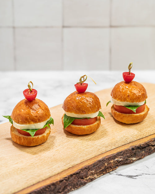 Trio of brioche sliders on a wooden plank. Filled with classic caprese