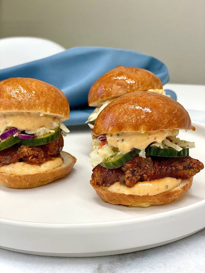 Trio of plated sliders with fried chicken on brioche buns with pickles, slaw, and spicy aioli