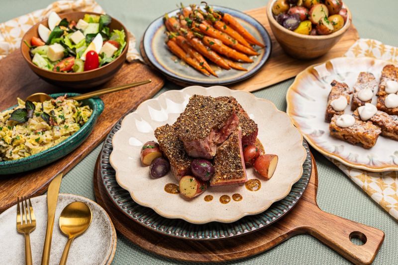 Platters of corn beef, Irish slaw, marbled potatoes, carrots, bread pudding, and mixed greens salad arranged in a package meal
