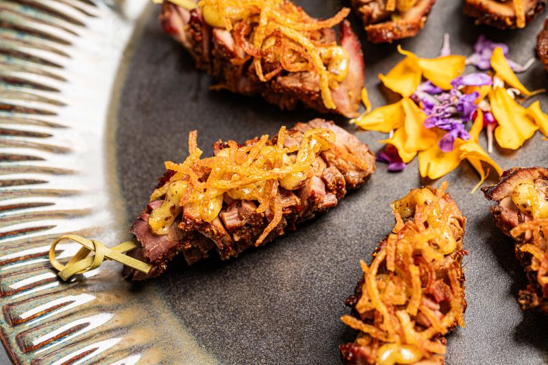 Gourmet hors d'oeuvre featuring beef skewer with crispy onions and house-made mustard sauce, ideal for cocktail receptions, corporate events, and wedding catering.