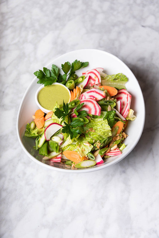 Shallow bowl of mixed greens, beets, carrots, snap peas, and Green Goddess dressing