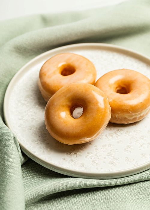 Mini glazed donuts on a textured white plate, with green linen underneath
