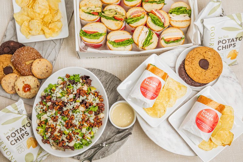 Sandwich halves, mixed greens salad with walnuts, assorted cookies, and kettle chips arranged in a package meal 