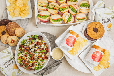 Sandwich halves, mixed greens salad with walnuts, assorted cookies, and kettle chips arranged in a package meal 