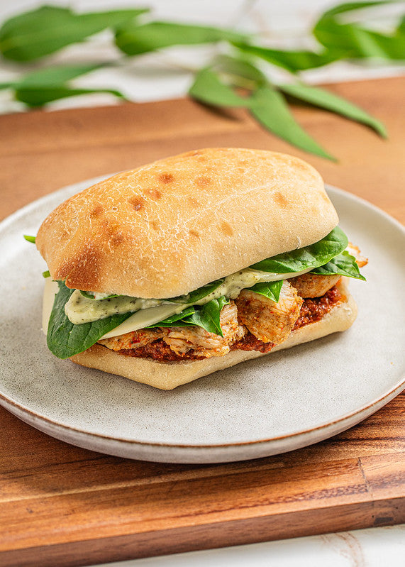 Ciabatta bread sandwich with sliced chicken, tomato pesto, herb aioli, and baby spinach 
