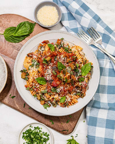 Fusilli pasta with ratatouille vegetables, plated with herb garnishes