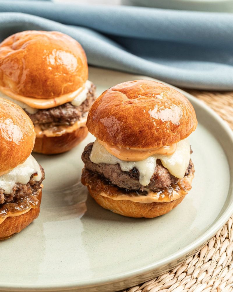 Trio of plated sliders with smash burger beef patty on brioche buns, with spicy aioli, caramelized onions, and white cheese