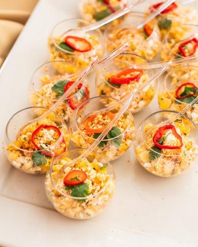 Platter with individual cups of street corn with cotjia , tajin, lime wedge ,and cilantro