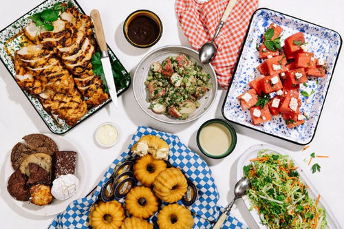 Picnic setup with barbecue chicken, potato salad, watermelon cubes, cornbread bundts, coleslaw, and cookies