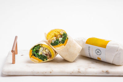 Breakfast burrito on a marble platter, cut in half exposing the vegan egg, potato, and spinach hash