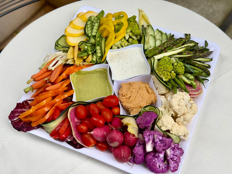 Assorted raw vegetables that include a trio of dips; mesquite smoked hummus, tzatziki sauce, green goddess dressing