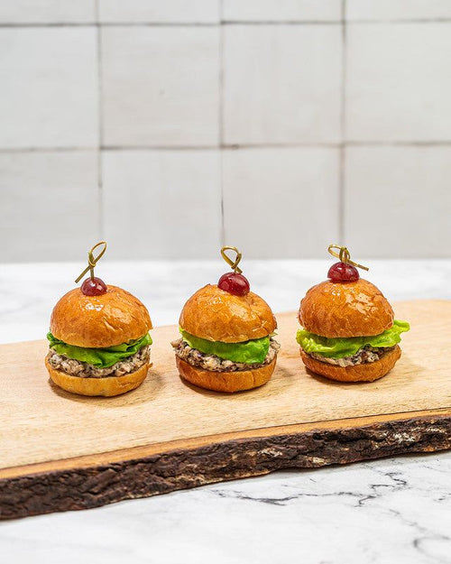 Trio of brioche sliders on a wooden plank. Filled with chicken salad