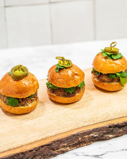 Trio of brioche sliders on a wooden plank. Filled with braised pork