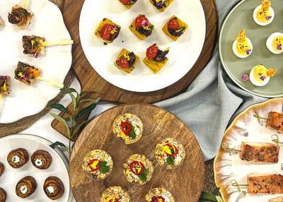 Assorted plattered appetiizers including corn cups, skewers of chicken and slamon, deviled eggs, and potato bites